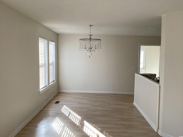 unfurnished dining area with a textured ceiling, light wood-style flooring, a notable chandelier, visible vents, and baseboards