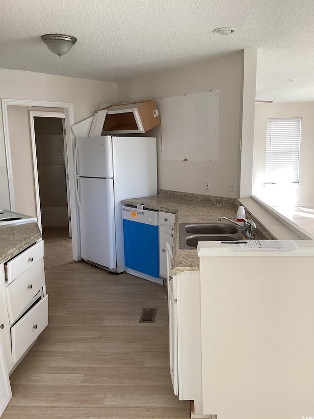 kitchen featuring dishwashing machine, a sink, visible vents, white cabinetry, and light wood finished floors