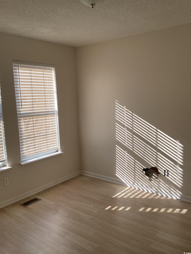 spare room with a textured ceiling, wood finished floors, visible vents, and baseboards