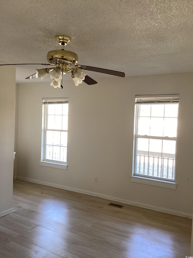 unfurnished room with a textured ceiling, wood finished floors, visible vents, and baseboards