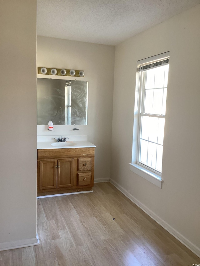 bathroom with a textured ceiling, vanity, baseboards, and wood finished floors