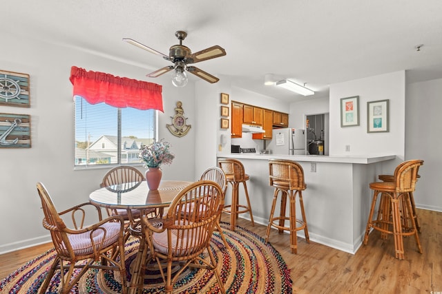 dining space featuring a ceiling fan, light wood-type flooring, and baseboards