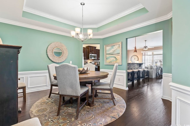 dining room featuring dark wood-style floors, a tray ceiling, a wainscoted wall, and a notable chandelier