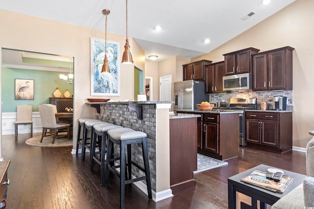 kitchen featuring a breakfast bar area, dark brown cabinets, appliances with stainless steel finishes, dark stone countertops, and decorative light fixtures