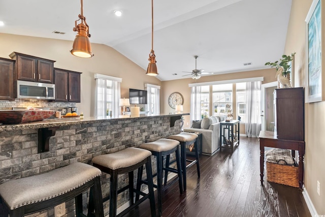 kitchen with lofted ceiling, stainless steel microwave, hanging light fixtures, dark brown cabinetry, and a kitchen breakfast bar