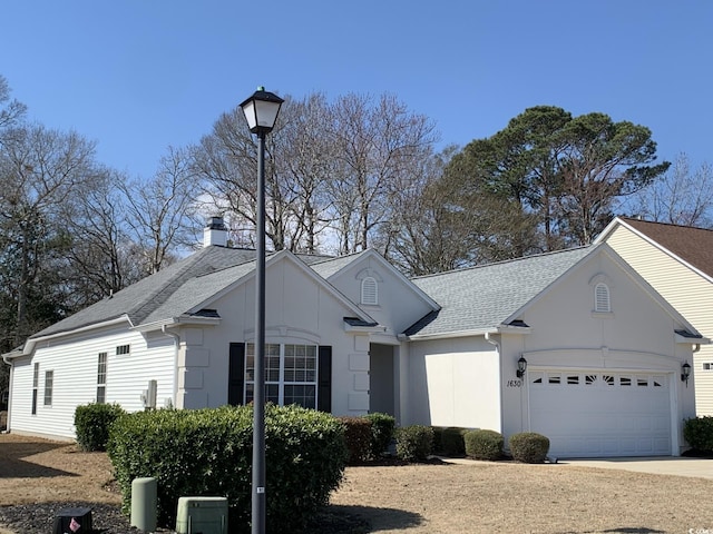 ranch-style home with a garage, a chimney, a shingled roof, and driveway