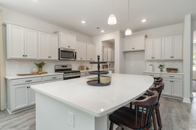 kitchen featuring appliances with stainless steel finishes, light wood finished floors, backsplash, a center island with sink, and light countertops