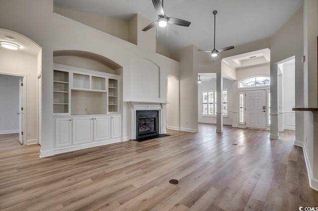 unfurnished living room with ceiling fan, high vaulted ceiling, a glass covered fireplace, and light wood-style floors