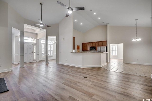 unfurnished living room with high vaulted ceiling, light wood-type flooring, and ceiling fan with notable chandelier