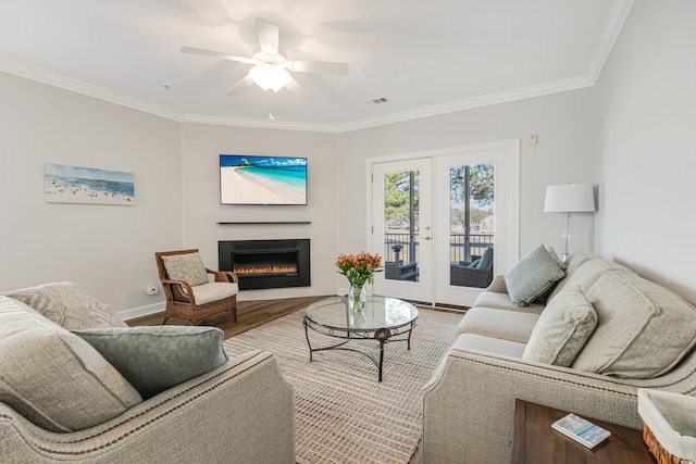 living area with french doors, visible vents, ornamental molding, wood finished floors, and a lit fireplace