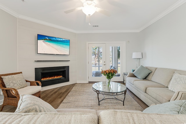 living area featuring ceiling fan, wood finished floors, visible vents, a glass covered fireplace, and crown molding