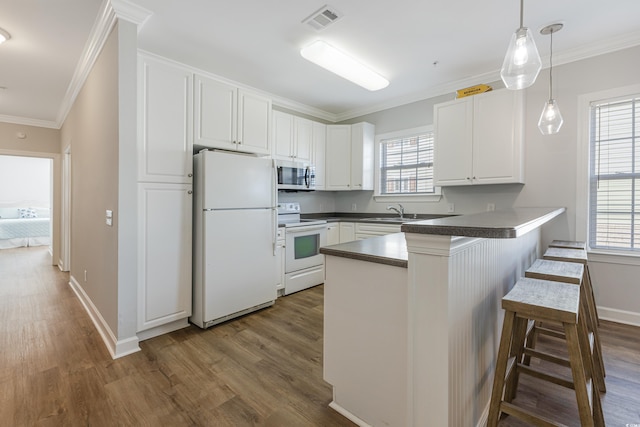 kitchen featuring a breakfast bar area, a peninsula, white appliances, white cabinets, and dark countertops