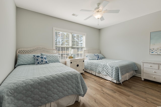 bedroom with ceiling fan, wood finished floors, visible vents, and baseboards