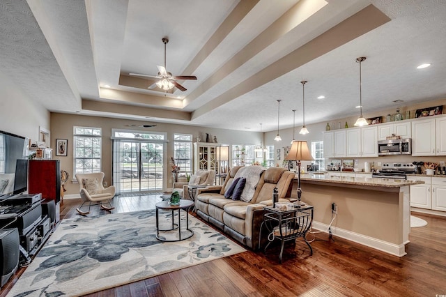 living room with baseboards, a textured ceiling, a tray ceiling, and dark wood-type flooring