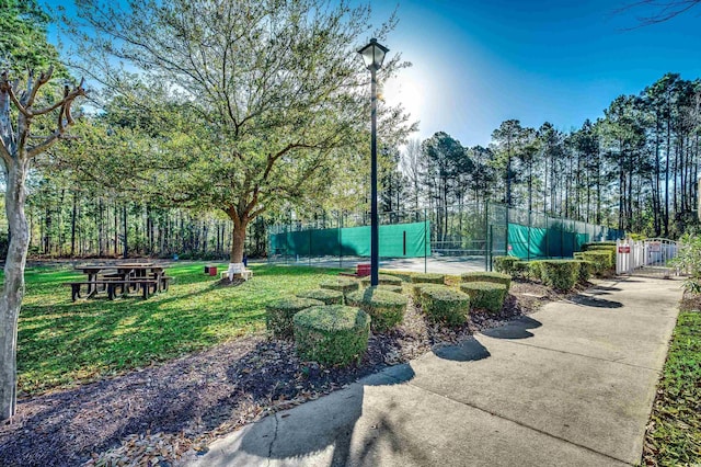 view of community with a tennis court, a yard, and fence