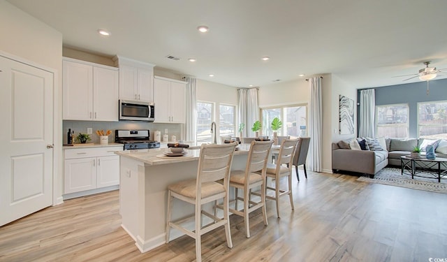 kitchen with light wood-type flooring, visible vents, an island with sink, tasteful backsplash, and appliances with stainless steel finishes