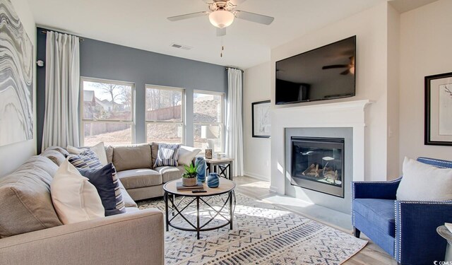 living area with visible vents, light wood-style flooring, a ceiling fan, and a fireplace with flush hearth