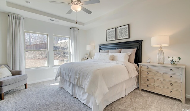 bedroom featuring visible vents, baseboards, light colored carpet, a tray ceiling, and a ceiling fan