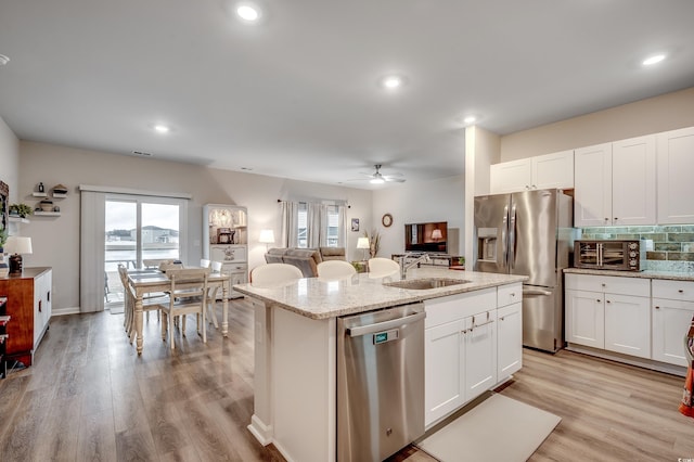 kitchen with backsplash, light wood-style flooring, appliances with stainless steel finishes, a sink, and an island with sink