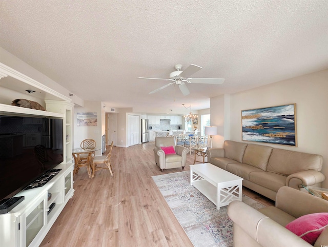 living room featuring ceiling fan with notable chandelier, light wood finished floors, and a textured ceiling