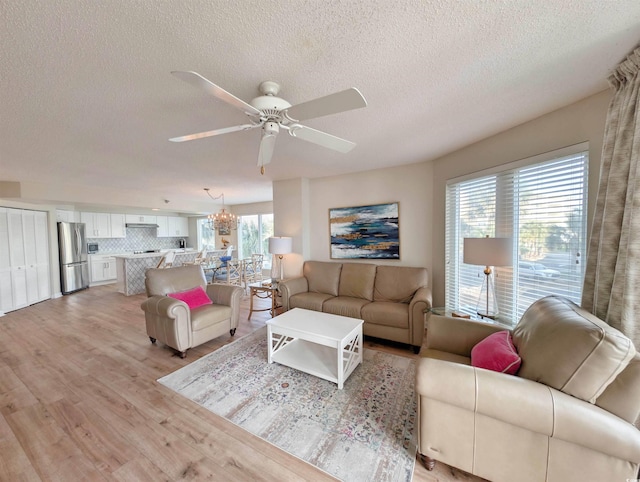 living room with light wood-style floors, a textured ceiling, and ceiling fan with notable chandelier