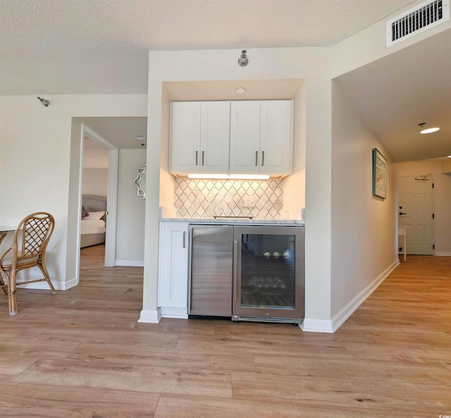 bar with beverage cooler, tasteful backsplash, visible vents, baseboards, and light wood-type flooring