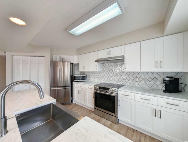 kitchen featuring stainless steel appliances, white cabinetry, a sink, light wood-type flooring, and under cabinet range hood