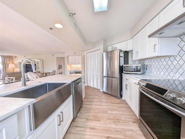 kitchen with stainless steel appliances, light stone countertops, white cabinets, and extractor fan