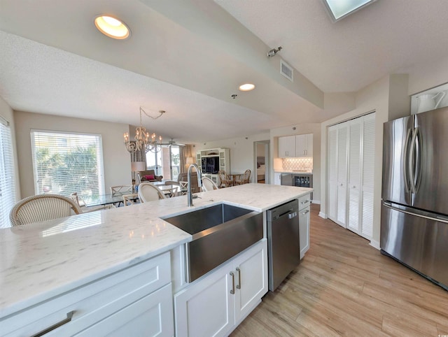 kitchen featuring light stone counters, a sink, white cabinetry, appliances with stainless steel finishes, and decorative light fixtures