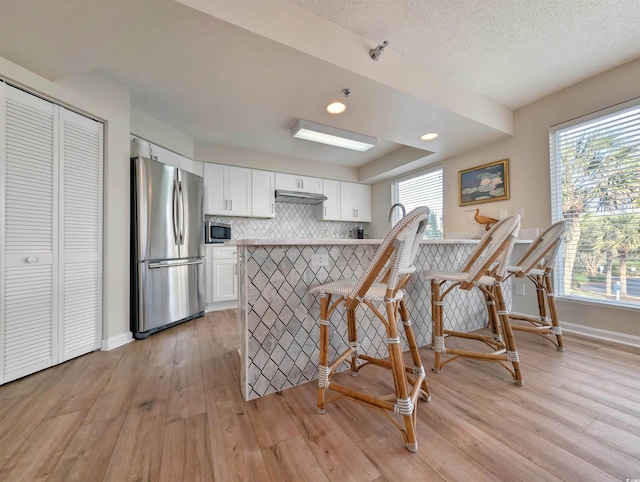 kitchen featuring under cabinet range hood, a peninsula, a breakfast bar, white cabinets, and appliances with stainless steel finishes