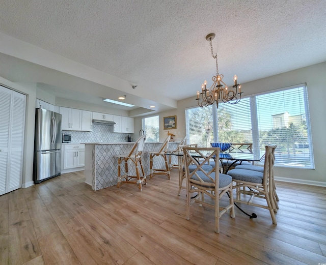 dining room with light wood finished floors, baseboards, a chandelier, and a textured ceiling