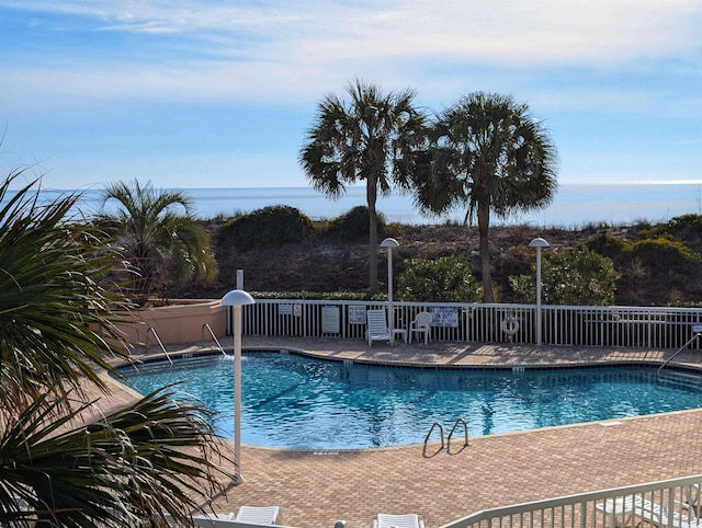 community pool with a water view, fence, and a patio