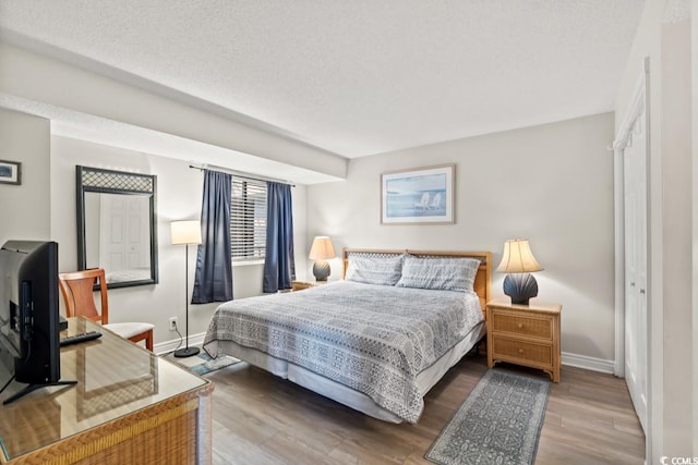 bedroom featuring a textured ceiling, baseboards, and wood finished floors