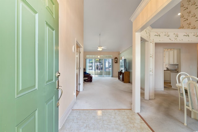 foyer with light tile patterned floors, light colored carpet, ornamental molding, a ceiling fan, and baseboards