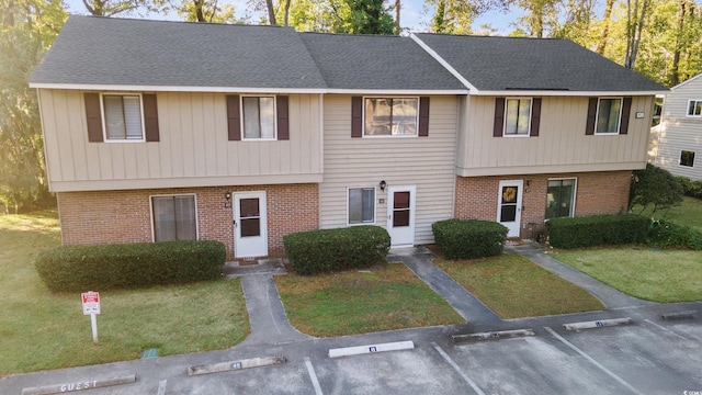 view of front of house with uncovered parking, a front yard, brick siding, and a shingled roof