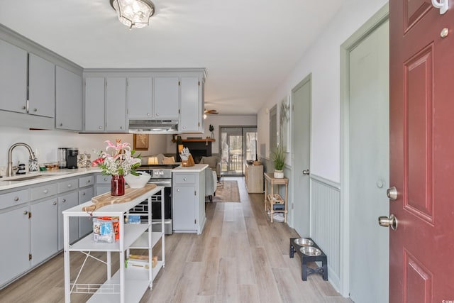 kitchen featuring stainless steel stove, under cabinet range hood, a sink, light wood-style floors, and light countertops