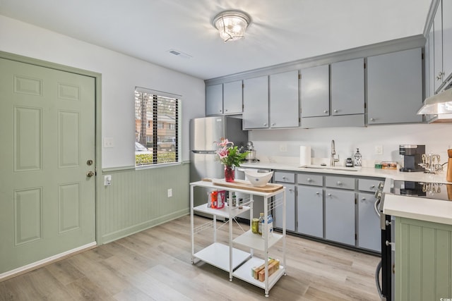 kitchen with a sink, light wood-style floors, light countertops, appliances with stainless steel finishes, and wainscoting