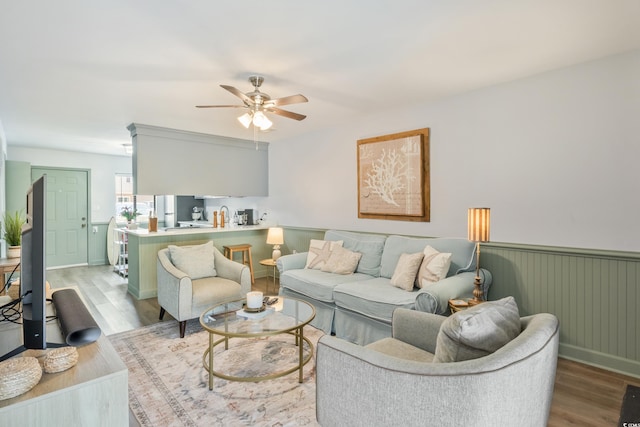 living area with a wainscoted wall, ceiling fan, and light wood finished floors