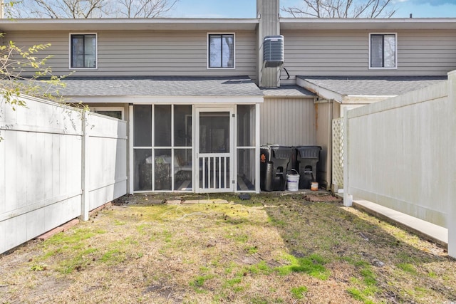 rear view of house featuring roof with shingles, a lawn, a fenced backyard, and a sunroom