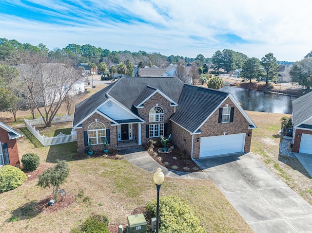 traditional-style home with brick siding, concrete driveway, a water view, fence, and a front yard