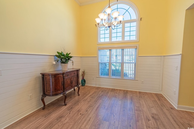 doorway with a wainscoted wall, wood finished floors, and a notable chandelier