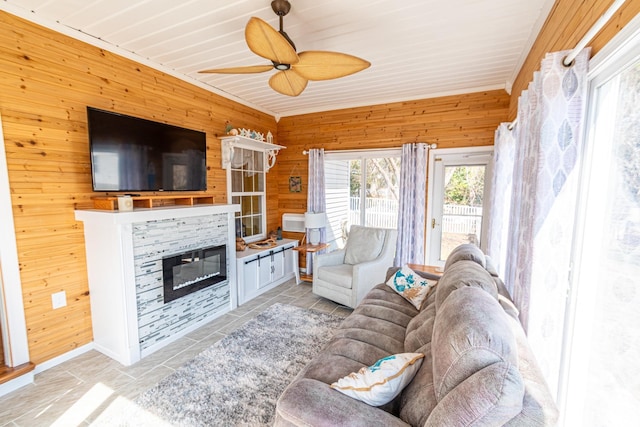 tiled living room with ceiling fan, wood walls, and a glass covered fireplace
