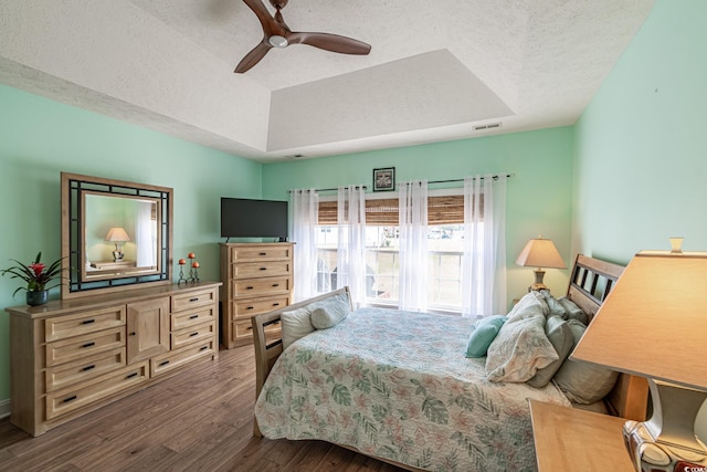 bedroom with wood finished floors, a textured ceiling, ceiling fan, a tray ceiling, and visible vents