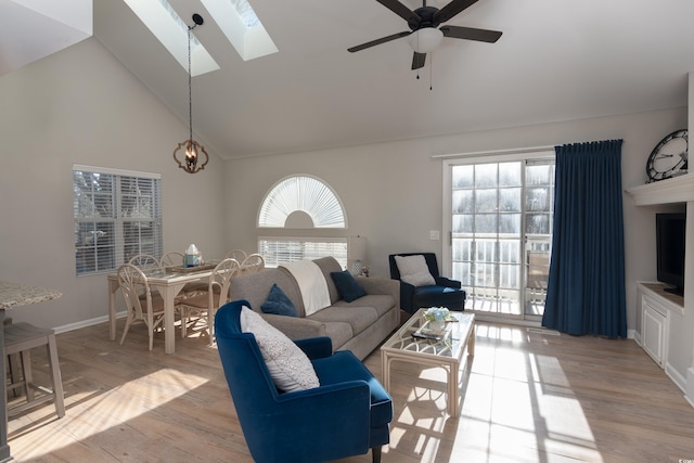 living room featuring light wood-style floors, high vaulted ceiling, a ceiling fan, baseboards, and a skylight
