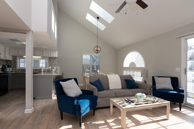 living area featuring light wood-style floors, high vaulted ceiling, a skylight, and ceiling fan with notable chandelier