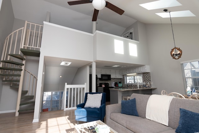 living area with plenty of natural light, high vaulted ceiling, ceiling fan, and light wood-type flooring