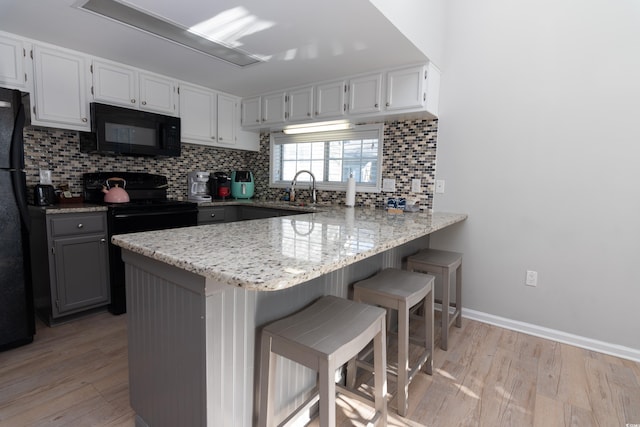 kitchen featuring a peninsula, backsplash, black appliances, and light wood finished floors