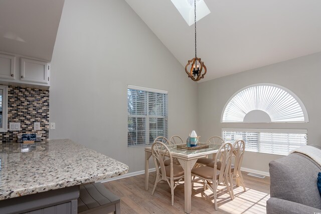 dining space featuring an inviting chandelier, light wood-style floors, baseboards, high vaulted ceiling, and a skylight