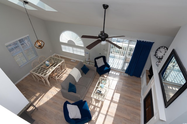 living area featuring vaulted ceiling with skylight, a ceiling fan, visible vents, wood finished floors, and baseboards