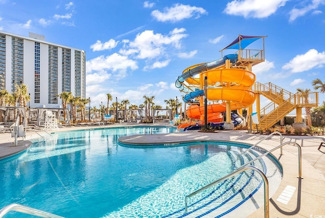 community pool with a patio, a water slide, stairs, and a water play area
